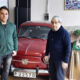 Dos hombres posan junto a un automóvil rojo clásico en un espacio con materiales de tapicería.