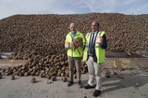 Dos hombres con chalecos reflectantes muestran remolachas ante una gran pila de tubérculos.