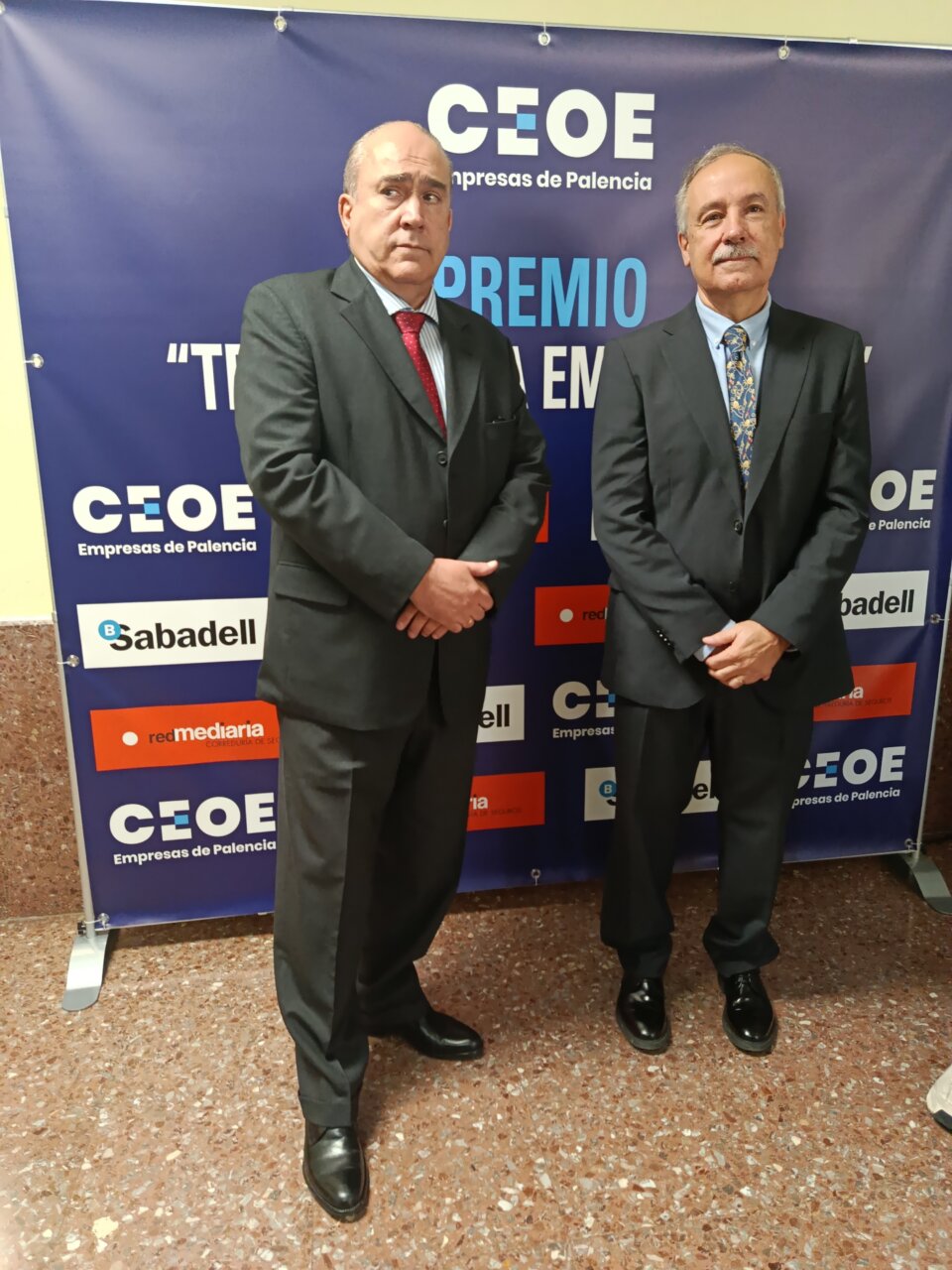 Dos hombres posan con traje ante un panel de CEOE Empresas de Palencia.