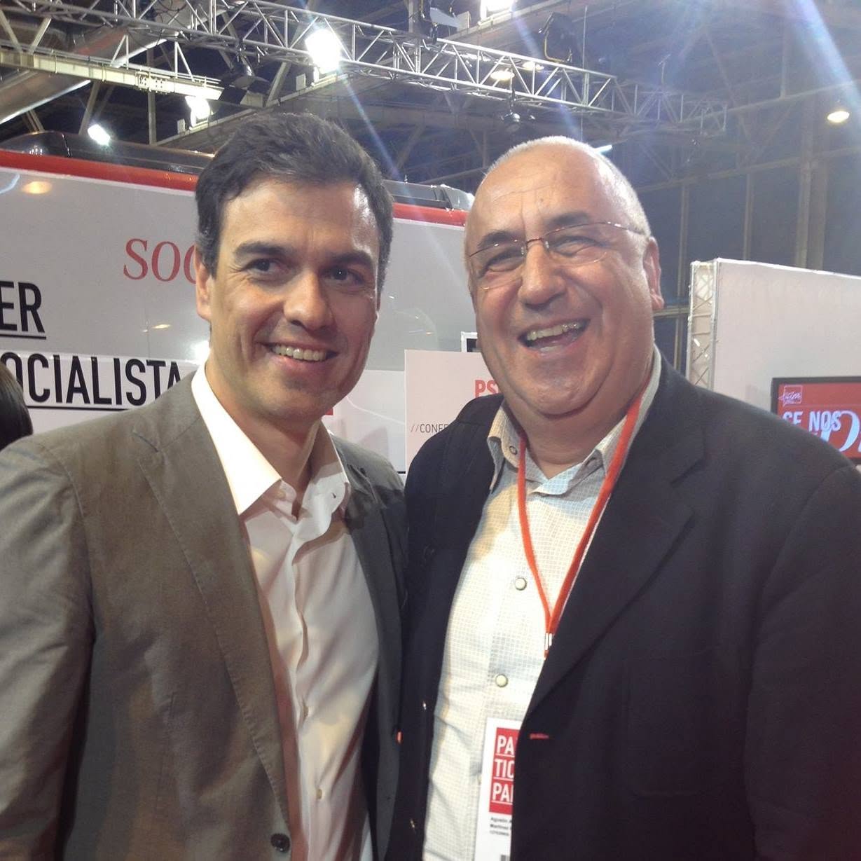 Dos hombres posan juntos frente a un fondo con carteles del PSOE