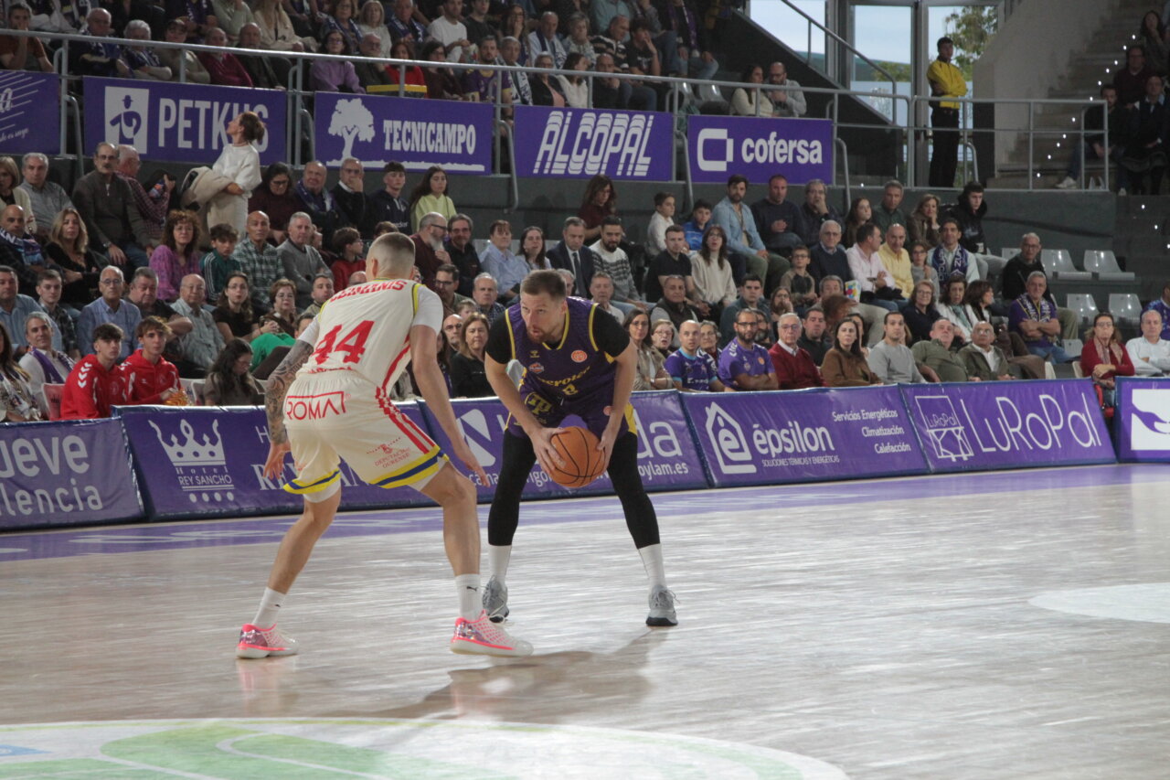 Un jugador de baloncesto con balón encara a un defensor ante las gradas llenas.