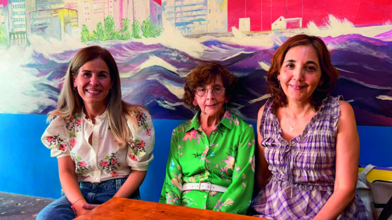 Tres mujeres sentadas en una mesa con fondo colorido