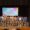 Grupo de participantes posa en el escenario bajo el cartel del evento solidario.