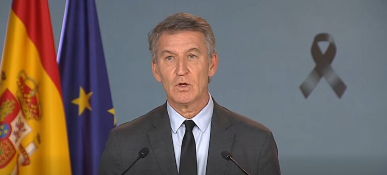 Alberto Núñez Feijóo habla ante dos micrófonos, con las banderas española y europea detrás.