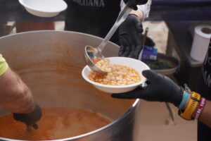 Una persona sirve alubias con un cucharón desde una olla grande en un cuenco.