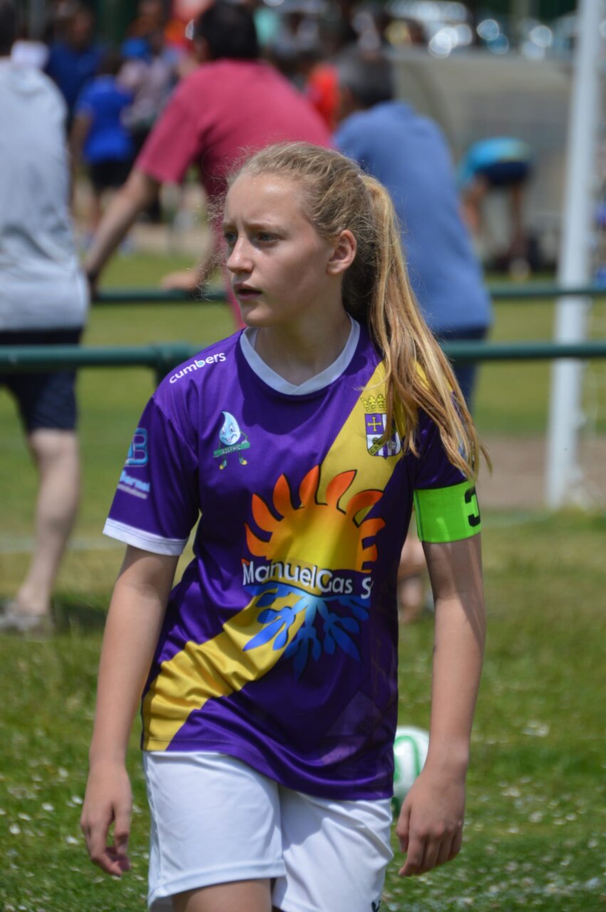 Futbolista con camiseta morada y brazalete verde en un campo de fútbol