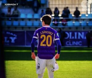 Fotografía de un futbolista de espaldas con camiseta morada y el número 20.
