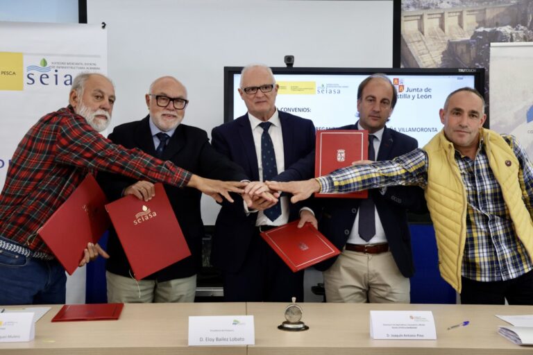 Cinco hombres posan con carpetas rojas y juntan las manos ante carteles institucionales.
