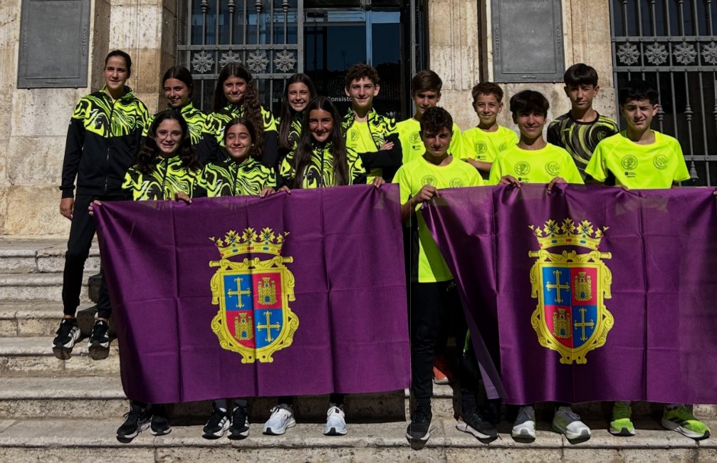 Jóvenes con ropa deportiva posan tras dos banderas moradas frente a un edificio