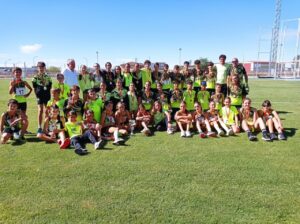 Grupo de jóvenes con medallas posa en un campo deportivo al aire libre.