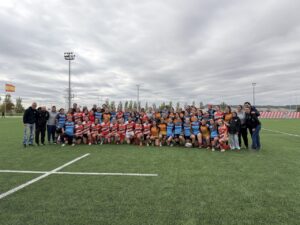 Grupo de jugadoras y acompañantes posa en un campo de rugby junto a un balón.