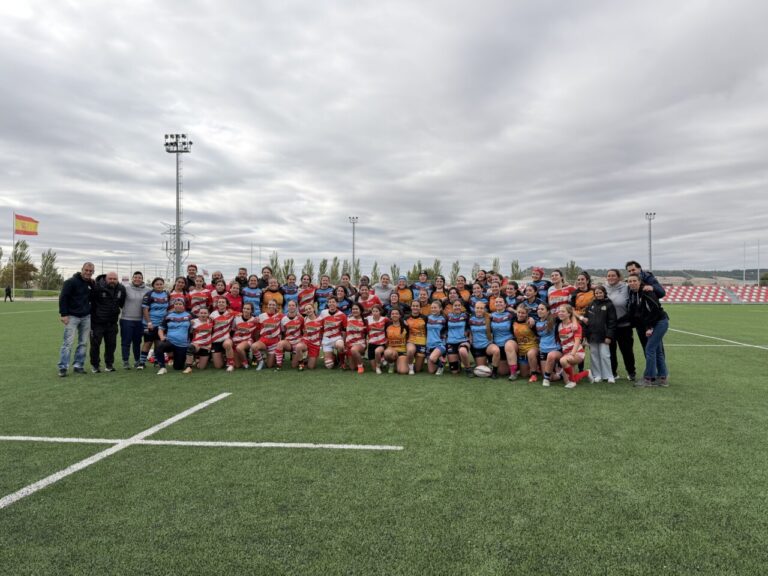 Grupo de jugadoras y acompañantes posa en un campo de rugby junto a un balón.