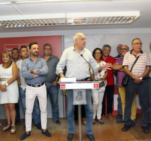 Un hombre habla desde un atril mientras varias personas posan a su alrededor