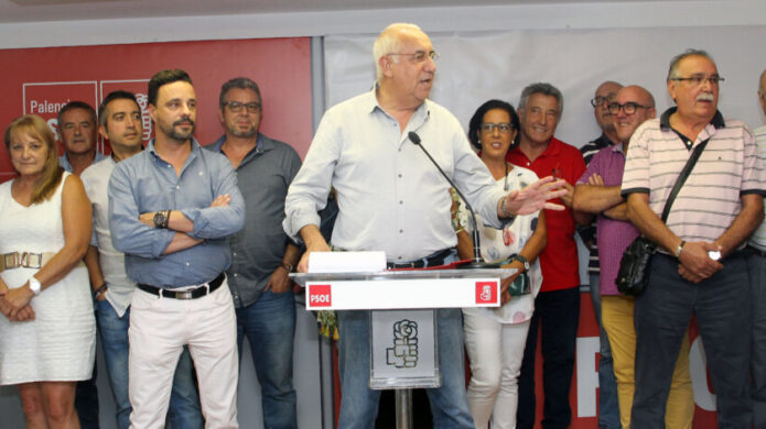 Un hombre habla desde un atril mientras varias personas posan a su alrededor