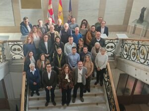 Grupo numeroso posa en una escalera interior ante varias banderas oficiales.