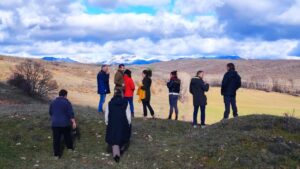 Varias personas recorren una ladera rural con campos y montañas al fondo