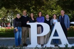 Siete personas posan al aire libre detrás de grandes letras blancas.