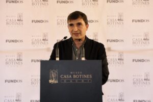 Hombre ante un atril del Museo Casa Botines, con logotipos de FUNDOS al fondo.