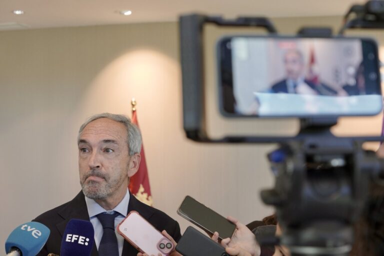Hombre con traje ante varios micrófonos y teléfonos durante una entrevista