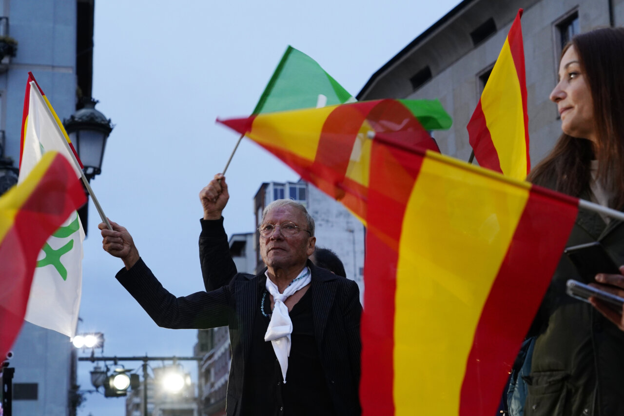 Un hombre sostiene una bandera española mientras varias banderas ondean a su alrededor.