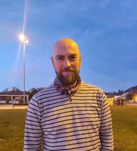 Hombre con camiseta a rayas y pañuelo posa en un parque al anochecer