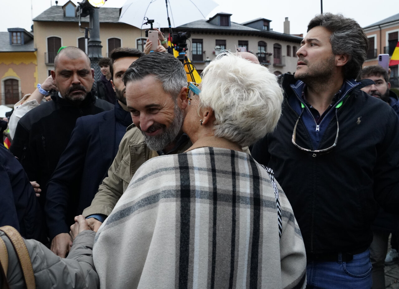 Un hombre de barba canosa saluda a una mujer mientras varias personas observan.