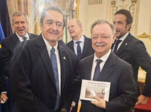 Dos hombres se estrechan la mano mientras uno sostiene el libro Imágenes postales de Palencia.