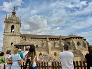 Visitantes contemplan la torre y los tejados de una iglesia de piedra.