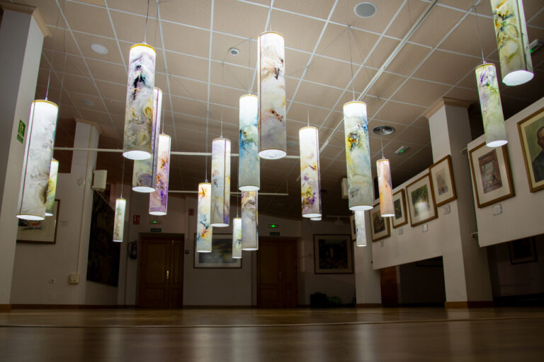 Instalación de acuarela con cilindros iluminados en una sala de exposición