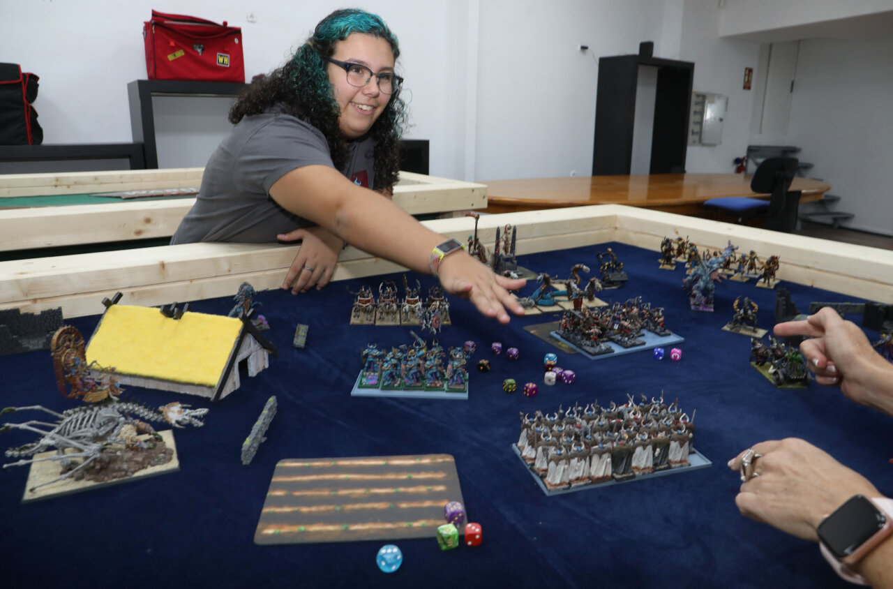 Una joven sonriente juega con miniaturas en una mesa de juegos.