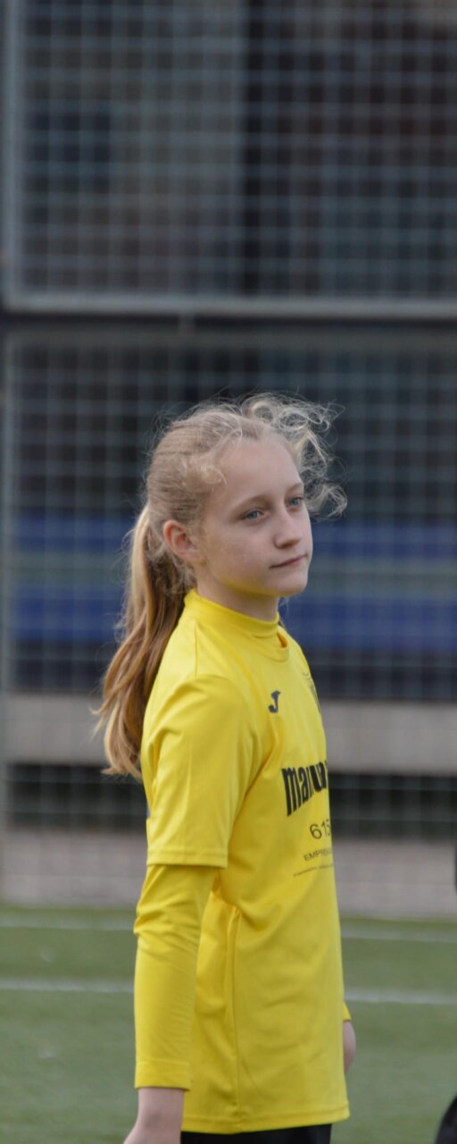 Joven con camiseta amarilla de fútbol, de pie ante una estructura de malla.