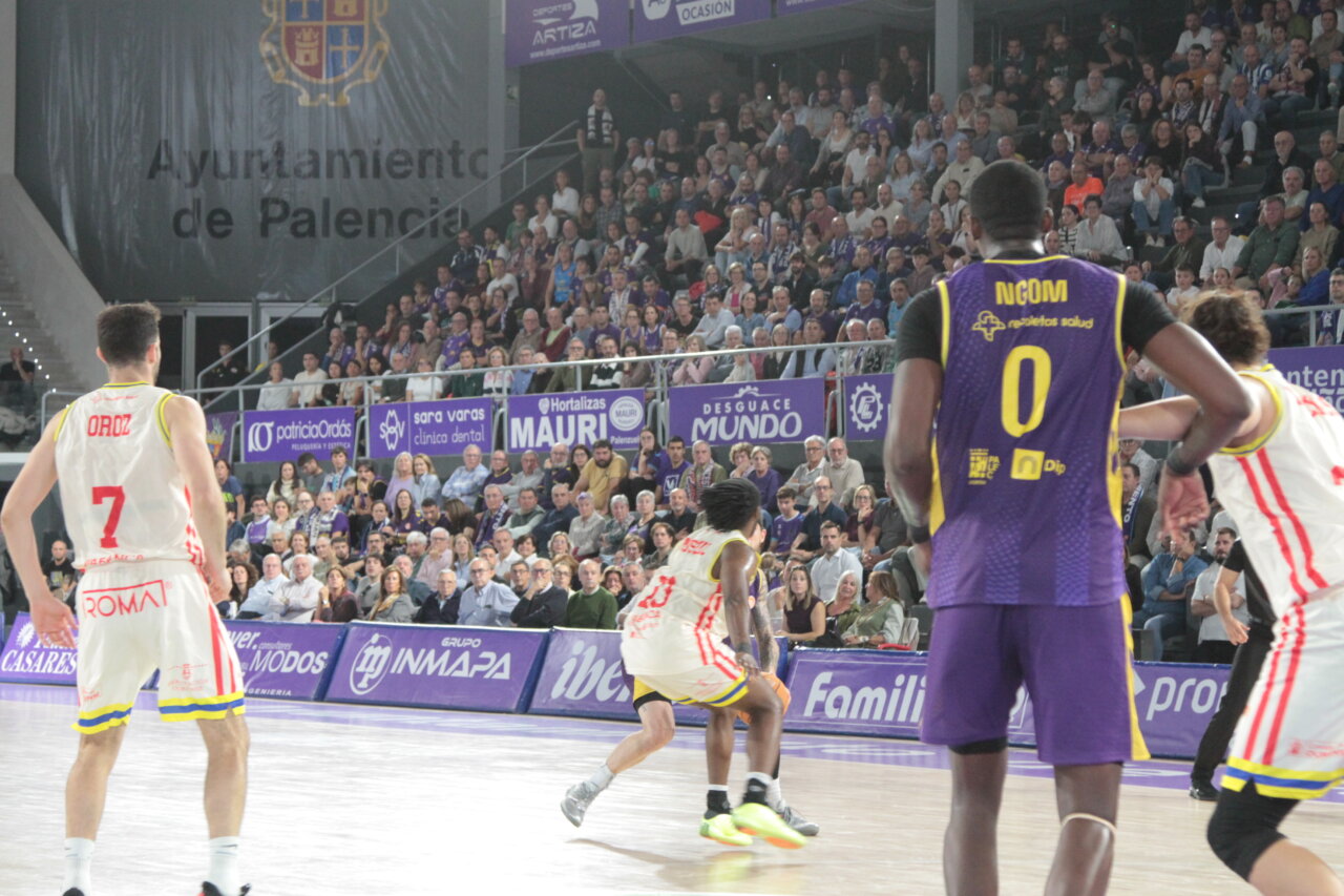 Jugadores de baloncesto disputan una jugada en una pista cubierta ante las gradas llenas.
