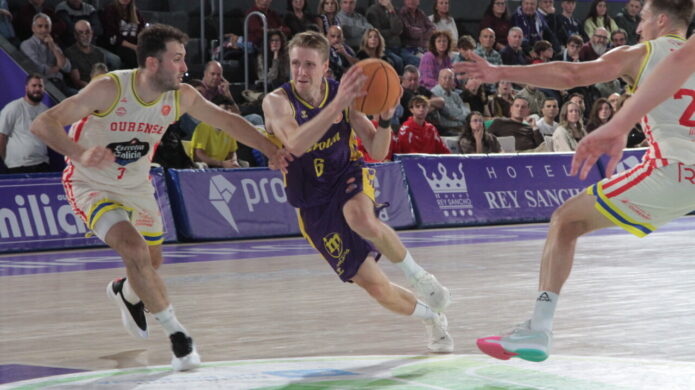 Jugador de baloncesto avanza con el balón mientras dos rivales intentan defenderlo.
