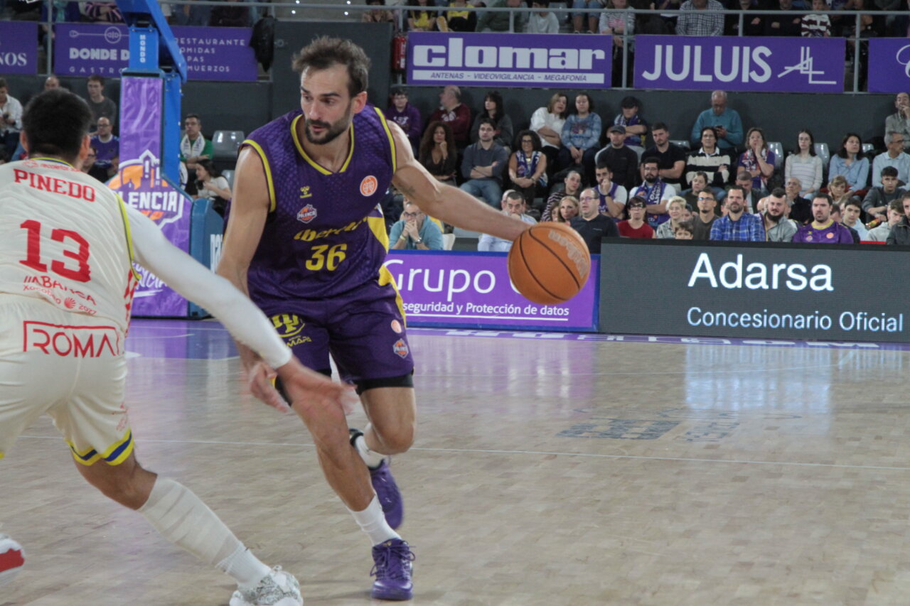 Jugador de baloncesto con camiseta morada bota el balón ante un rival.
