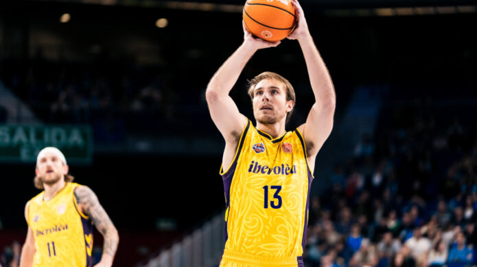 Jugador de baloncesto con uniforme amarillo prepara un lanzamiento mientras otro espera detrás.