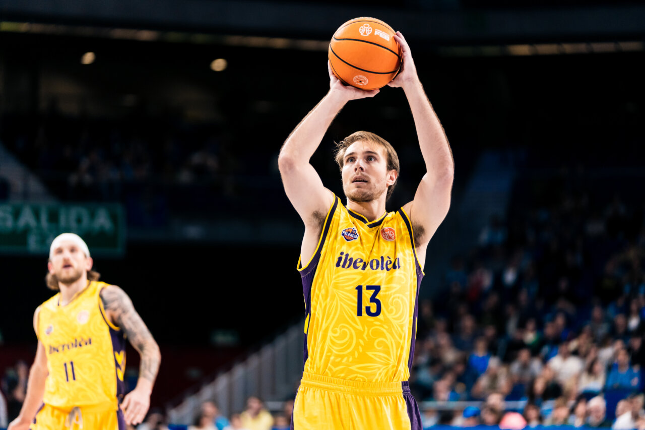 Jugador de baloncesto con uniforme amarillo prepara un lanzamiento mientras otro espera detrás.