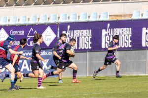 Jugador de rugby corre con el balón mientras varios jugadores lo siguen en el campo.