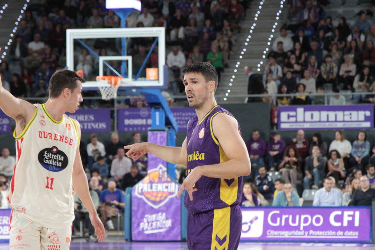 Dos jugadores de baloncesto se enfrentan en una cancha cubierta con gradas llenas