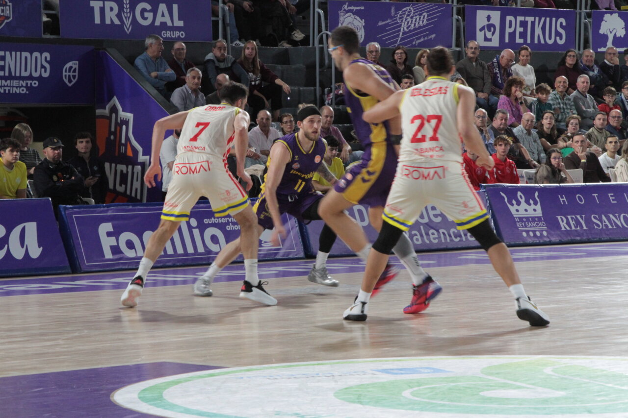 Fotografía de jugadores de baloncesto disputando una jugada en una cancha cubierta ante el público.