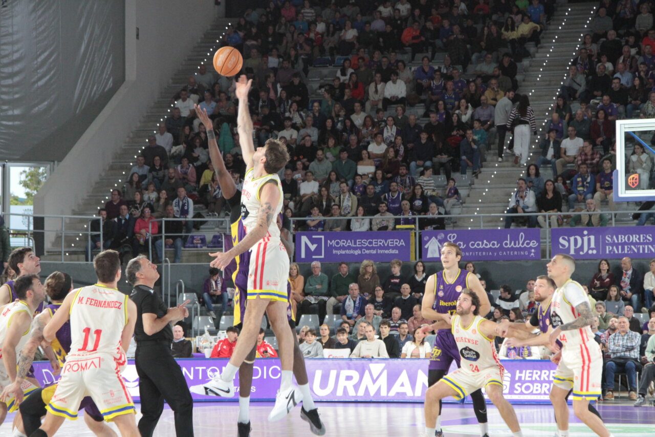 Dos jugadores de baloncesto saltan para alcanzar el balón ante el público.