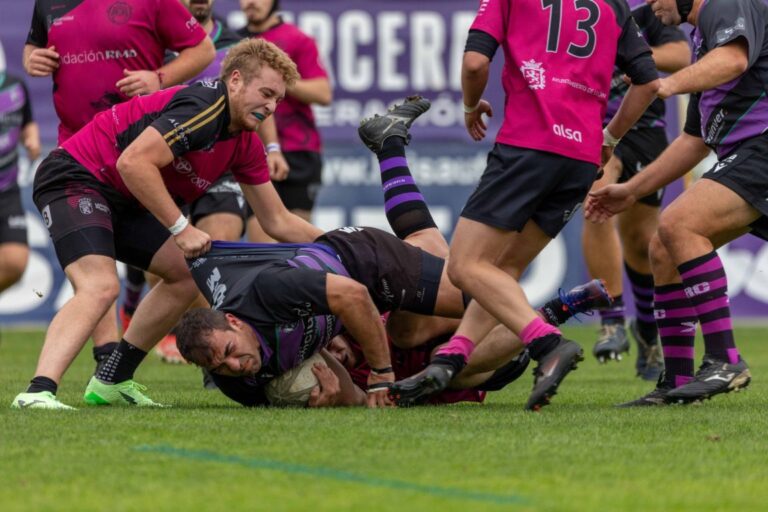 Jugador de rugby con el balón mientras rivales intentan derribarlo en el césped.