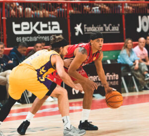 Dos jugadores disputan un balón durante un partido de baloncesto en una cancha.