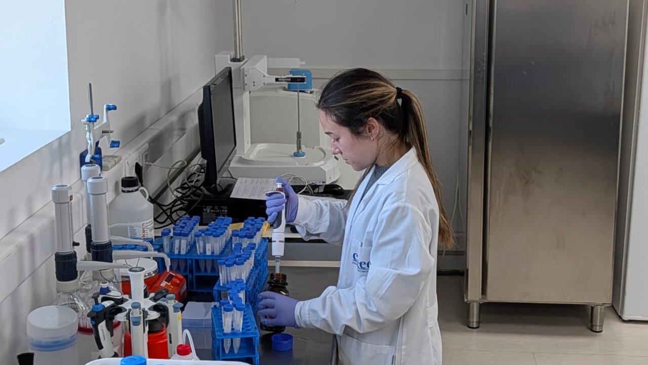 Una persona con bata manipula una pipeta junto a tubos de ensayo en un laboratorio.