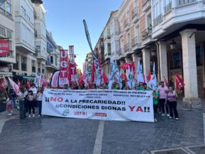 Manifestantes sostienen una pancarta y banderas sindicales en una calle peatonal de Palencia.