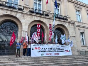 Manifestantes sostienen una pancarta sobre condiciones dignas frente a un edificio de piedra.