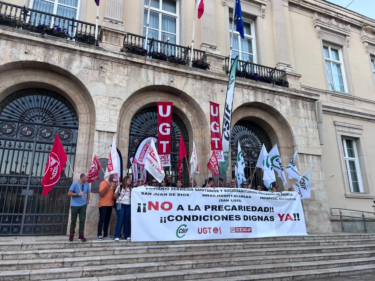 Manifestantes sostienen una pancarta sobre condiciones dignas frente a un edificio de piedra.
