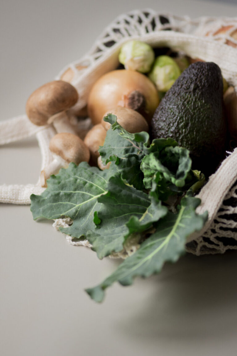 Verduras frescas en una bolsa de malla, incluyendo aguacate y champiñones.