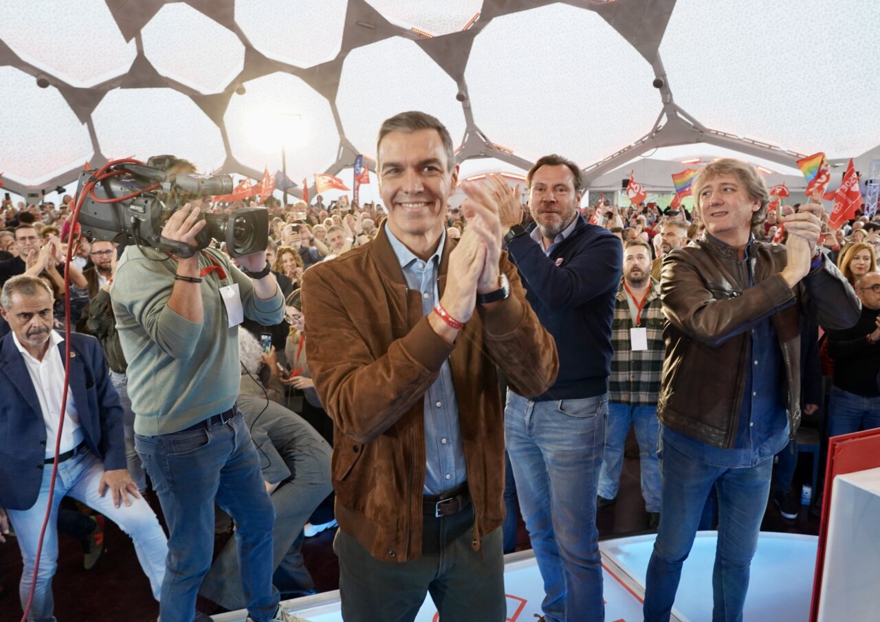 Pedro Sánchez aplaude frente a una multitud durante un acto político bajo una cúpula geométrica.