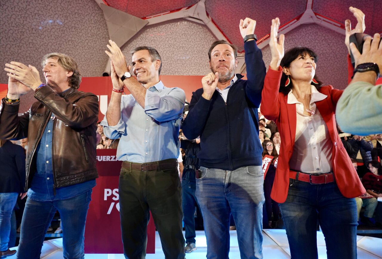 Pedro Sánchez y otras personas aplauden sobre un escenario ante el público.