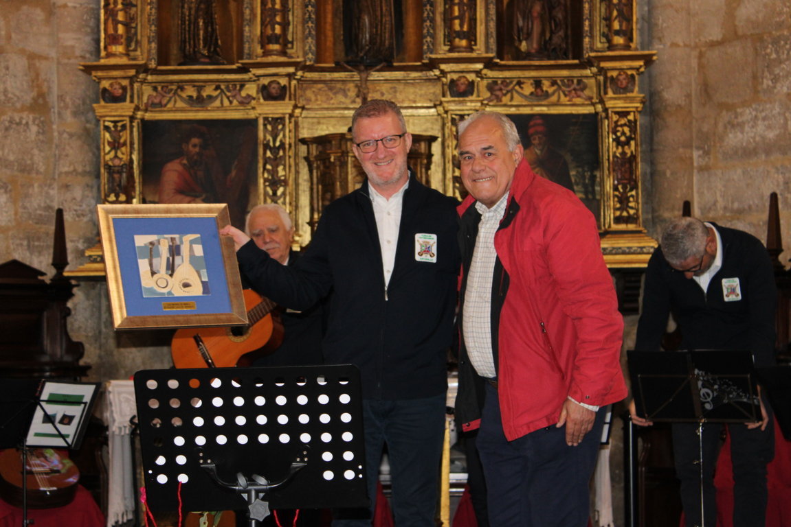 Dos hombres posan junto a un marco, con músicos e instrumentos ante un retablo ornamentado.